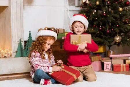 Kids wearing Christmas pajama opening gifts in front of Christmas tree in the living room