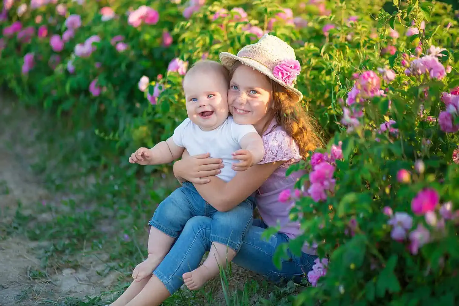 Cute siblings sitting in pink rose field bush
