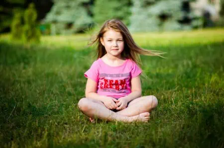 Pretty little girl in pink top sitting on grass