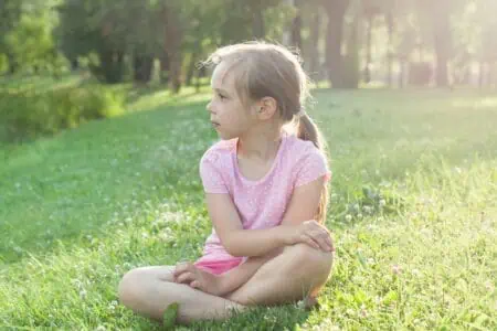 Little girl wearing pink t-shirt sitting on the grass at the park