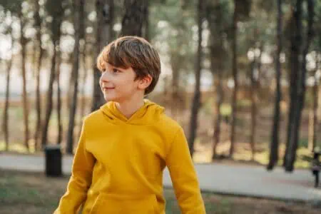Adorable young boy in yellow jacket against forest background
