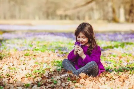 Little girl wearing violet blouse sitting on the grass outdoors
