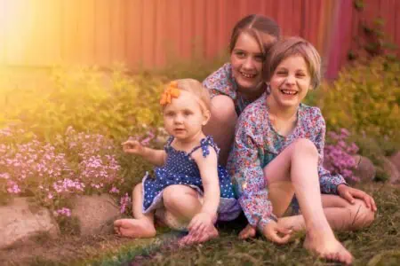 Three adorable sisters sitting on the grass near the country house