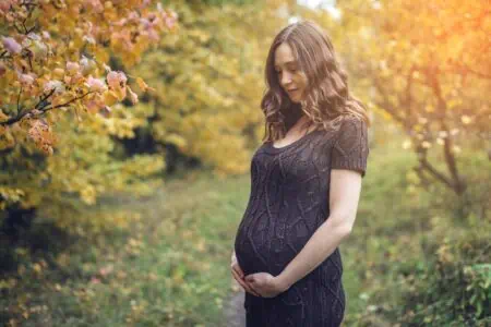 Pregnant woman holding her belly spending time at the park during autumn season