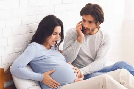 Pregnant woman in pain with her worried husband sitting on the couch