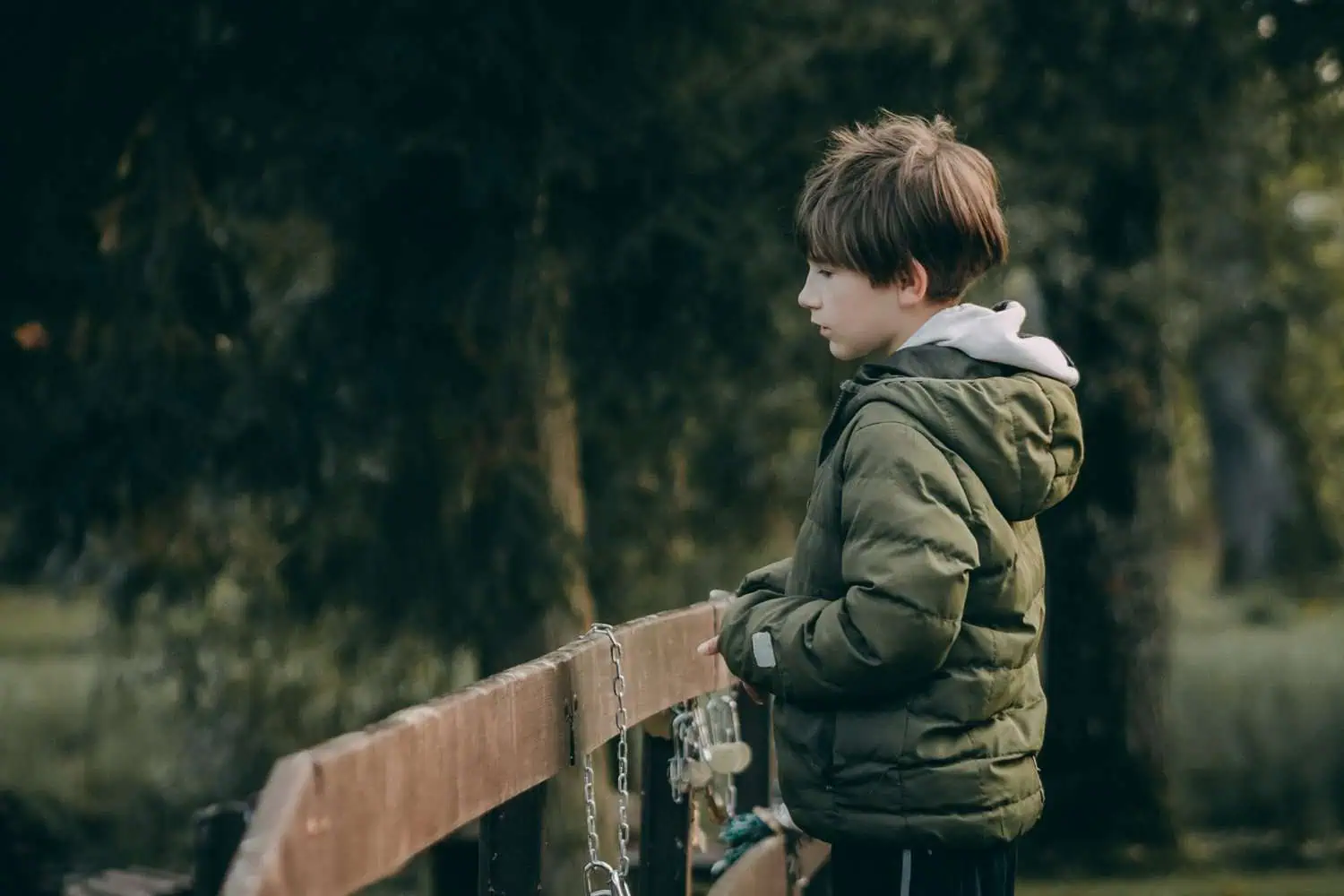 Adorable young boy wearing jacket standing near wooden fence at the park