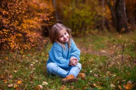 Cute little girl in blue sitting on green grass in autumn park