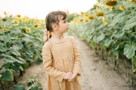 Beautiful young girl in summer dress standing in sunflower field