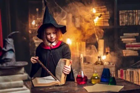 Little girl in witch Cosplay costume pointing wand at a book
