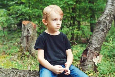 Young boy sitting on tree log in the forest