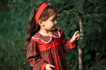 Little girl in red dress touching Christmas tree with her finger