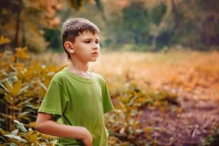 Young boy in green shirt standing at an autumn park
