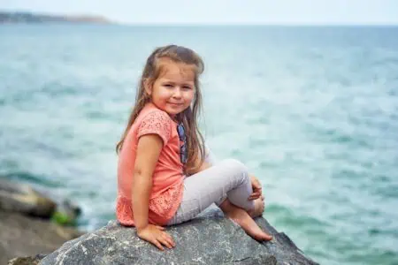 Beautiful little girl sitting on the rock near the sea coast