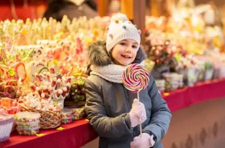 Little girl with lollipop standing in front of candy shop at christmas market