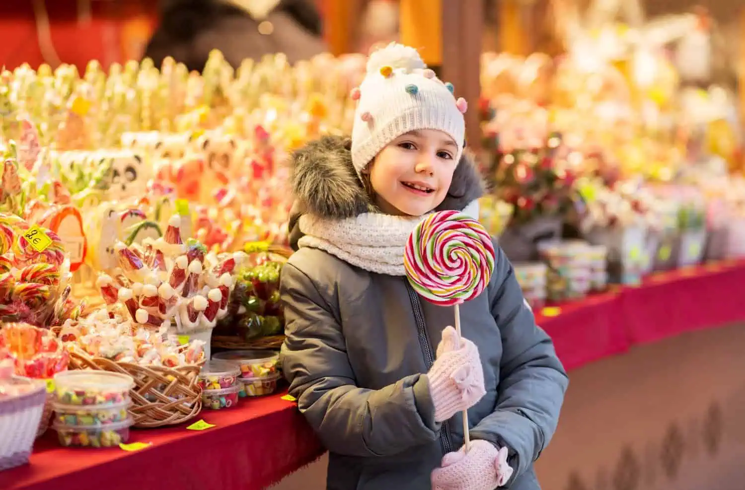 Little girl with lollipop standing in front of candy shop at christmas market