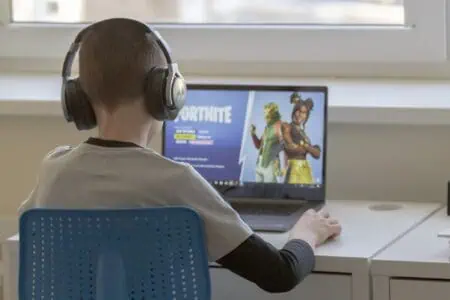 Little boy with headphones playing fortnite oh his laptop