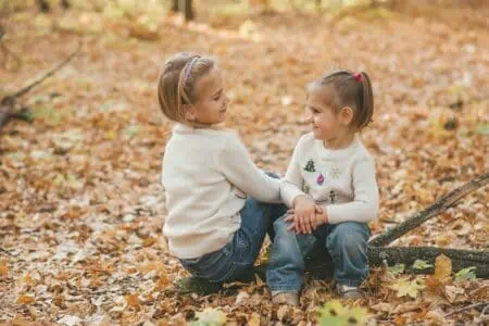 Happy sisters looking at each other while sitting on the log at autumn park