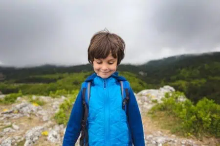 Young boy wearing backpack standing on top of the mountain with nature background