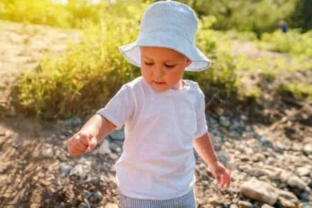 Adorable little boy child wearing hat playing with rocks on sunny day