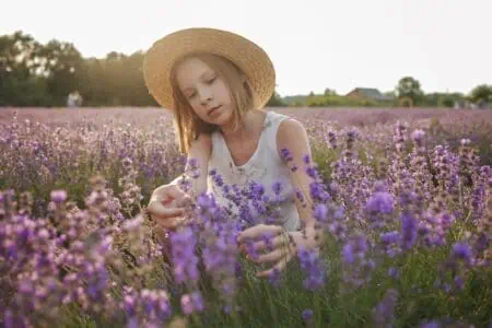 Young girl wearing straw hat sitting in lavender field