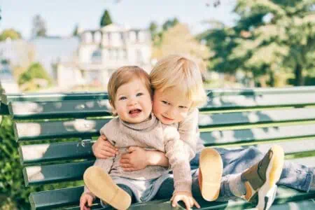Adorable siblings resting on the bench in sunny park