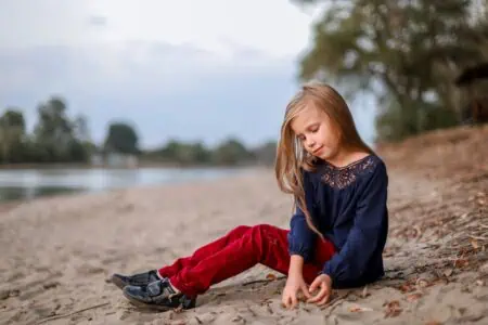 Pretty young girl in red pants sitting on the sand at the beach