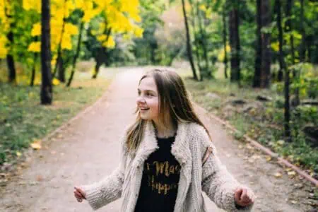 Smiling little girl walking in the forest at autumn day