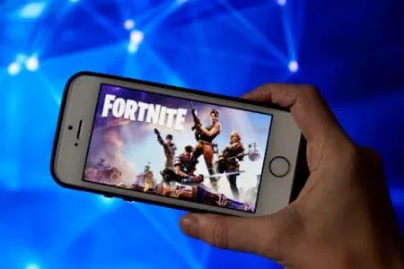 A man's hand holding a phone showing Fortnite game