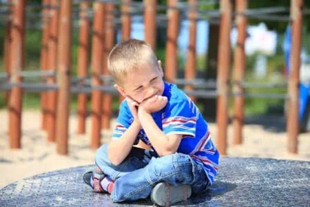 Caucasian young boy sitting on the round metal platform at the playground