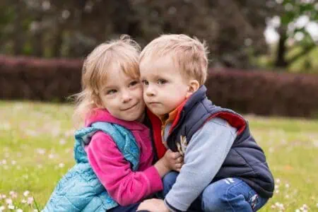 Sweet sibling sitting on the grass at the park while hugging each other