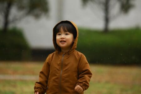 Korean little boy wearing brown jacket standing outdoors while drizzling