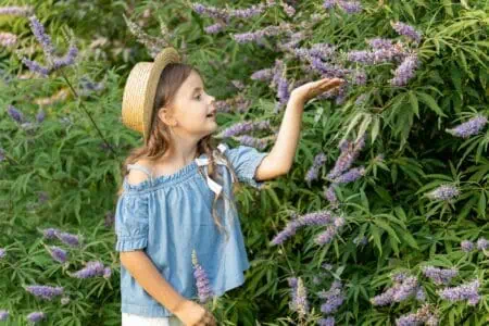 Little girl wearing straw hat touching flower in the garden
