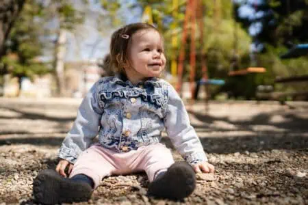 Little girl in denim jacket sitting on the ground at the playground