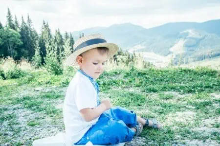 Adorable little boy wearing summer hat sitting on the ground on top of the mountain