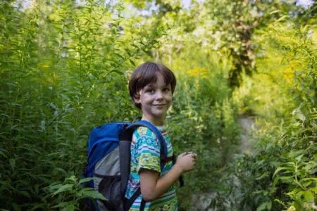 Young boy with a backpack standing among the trees in the meadow