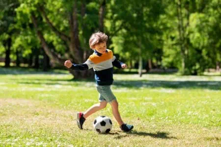 Happy little boy playing soccer at summer park