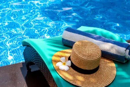 Towel and summer hat with flower on top of lounge chair by the pool