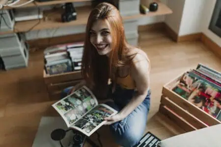 Cheerful young woman smiling at camera while sitting on the floor holding an open comic book